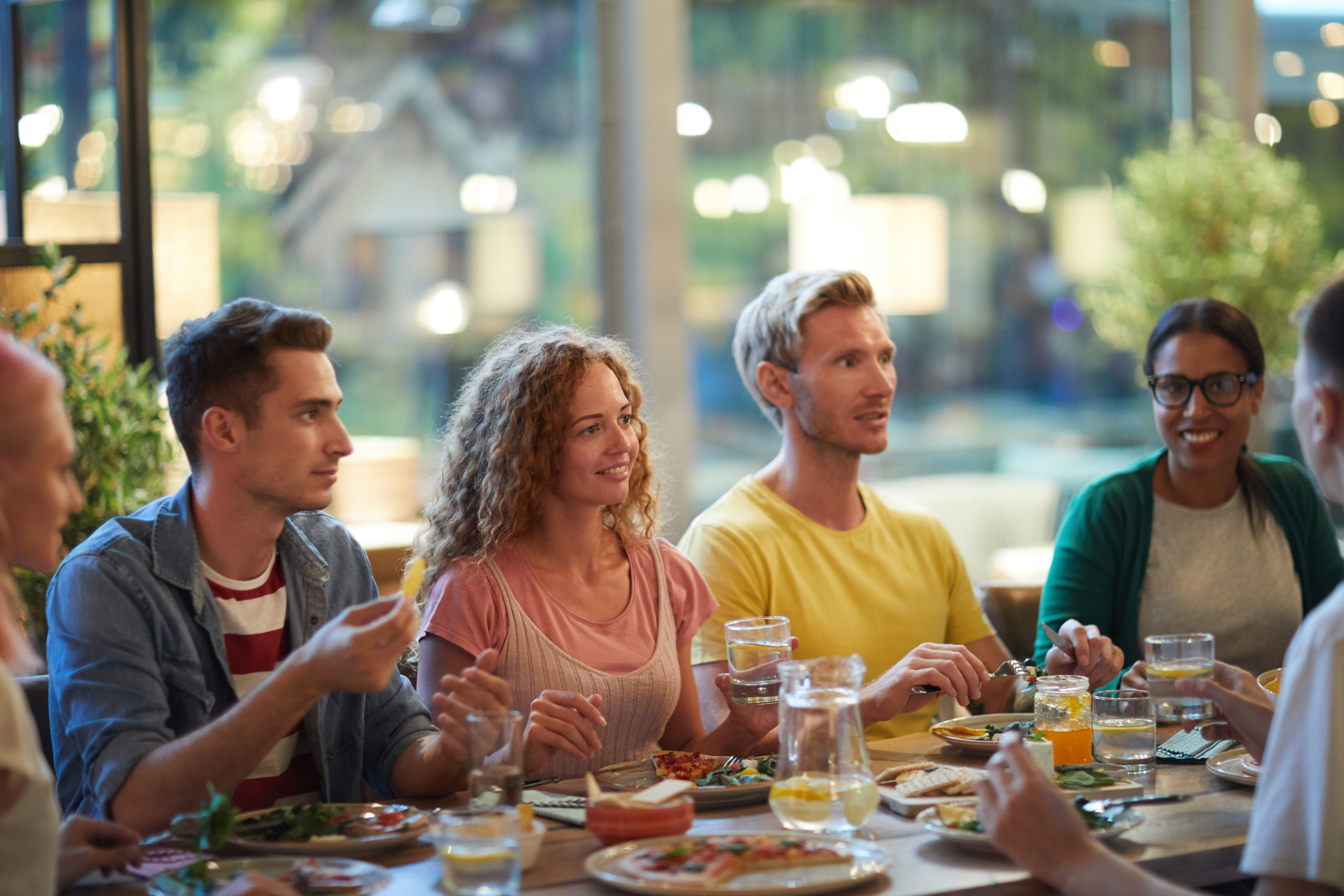 Cheerful young friends enjoying meals in restaurant and discussing curious things by dinner